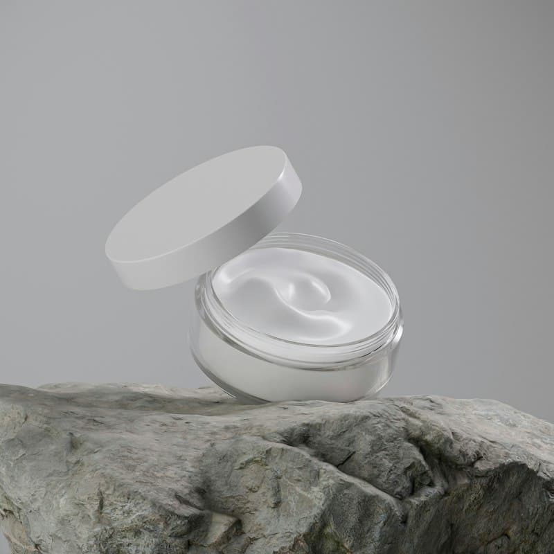 An open glass jar of white cream resting on a grey stone