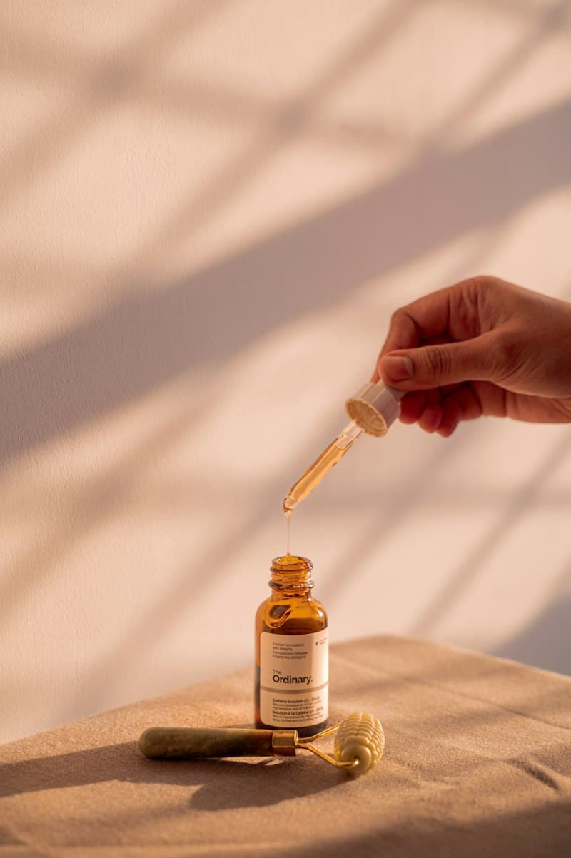A hand lifting a dropper from a small amber bottle in soft window light