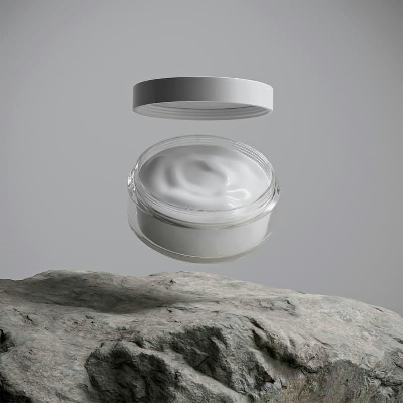 A jar of white cream with its lid floating above it over a stone