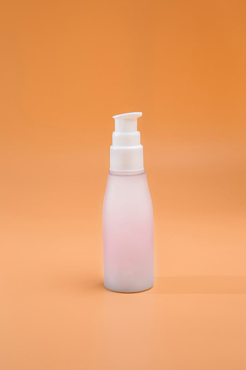 A frosted pump bottle against a warm orange background