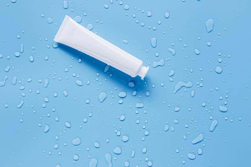 A plain white tube lying on a blue surface scattered with water drops