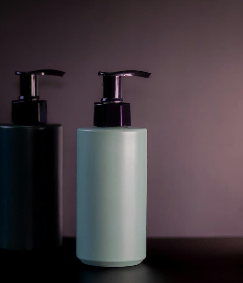 Two plain pump bottles, one dark and one pale blue, against a mauve wall